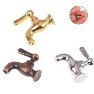 May include: Three miniature faucet charms in gold, bronze, and silver tones. The gold faucet is shiny, the bronze has a rustic finish, and the silver is polished. A small, similar charm is held in a hand in the upper right corner.