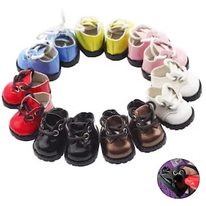 Può includere: Una collezione di scarpe in miniatura in vari colori, tra cui rosso, nero, marrone, bianco, rosa, giallo e blu. Ogni scarpa ha lacci e una piccola punta arrotondata. Le scarpe sono disposte in un motivo circolare.