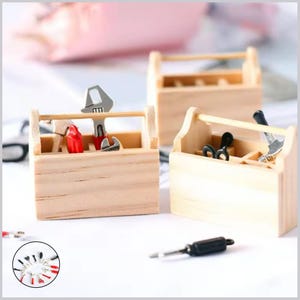 May include: Small wooden toolboxes, each containing miniature tools such as spanners, pliers, and screwdrivers. The toolboxes are light brown and have a handle. A small collection of additional tools is visible in a circle at the bottom left.