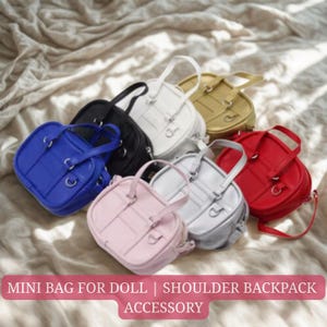 Puede incluir: Una colección de mini bolsos para muñecas en varios colores: azul, negro, blanco, dorado, rojo, rosa y plateado. Cada bolso tiene un asa superior y correas ajustables. Los bolsos están colocados sobre una superficie suave y texturizada.