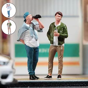 May include: Miniature figurines of two people, one drinking from a black bottle, the other holding a clear bottle. The first figure wears a blue cap, jeans, and a white shirt. The second figure wears a green jacket, tan pants, and a white shirt.