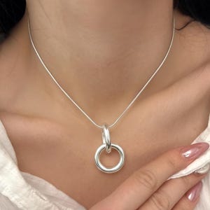 Peut inclure: Un collier argenté avec un pendentif composé de deux anneaux entrelacés. Le collier a une chaîne fine et une finition polie, créant un look minimaliste et élégant. Le bijou est conçu pour un usage quotidien.