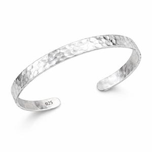 Op de afbeelding: Een zilveren manchetarmband met een gehamerde textuur. De open armband is gemaakt van glanzend metaal en heeft een getextureerd oppervlak. De armband is aan de binnenkant gemarkeerd met "925".