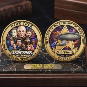 May include: Two circular commemorative coins featuring Star Trek: The Next Generation imagery. One side displays the cast, the text 'Star Trek The Next Generation 40th Anniversary 1987-2027'. The other shows the U.S.S. Enterprise NCC-1701-D, the text 'To Boldly Go Where No One Has Gone Before'.