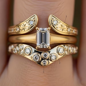 Puede incluir: Un conjunto de anillos de oro con detalles de diamantes. El anillo superior tiene un diseño de estrella y pequeños diamantes. El anillo del medio es una banda simple. El anillo inferior tiene un diseño curvo con múltiples engastes de diamantes.