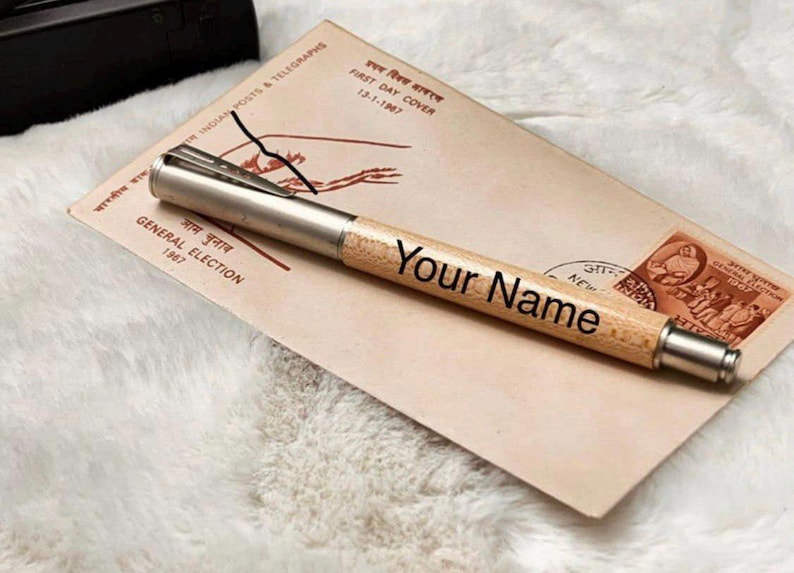 May include: A personalised pen with a light wood barrel and silver accents, inscribed with "Your Name." The pen rests on a vintage envelope with Indian postal markings and the text "GENERAL ELECTION 1967."