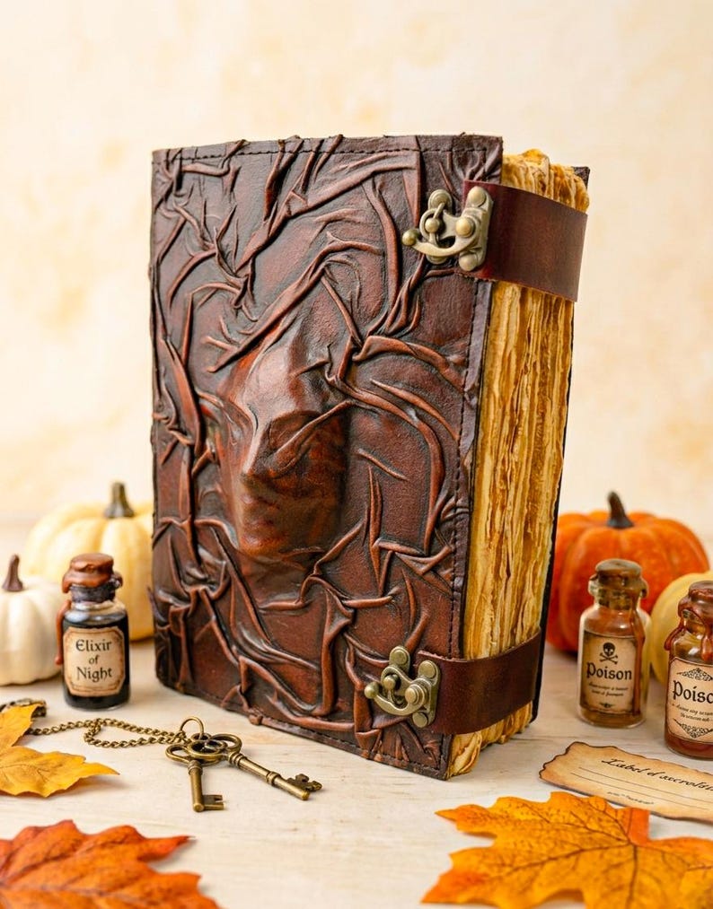 May include: A brown leather-bound book with a textured cover and a clasp closure. The book has a leather strap and aged pages. Decorative elements include small potion bottles, keys, and pumpkins, creating a Halloween theme.