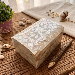 May include: A rectangular storage box featuring an intricate inlay of iridescent mother-of-pearl pieces. The lid displays a central floral motif surrounded by a geometric lattice pattern, while the sides are covered in a mosaic of shell fragments.