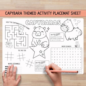 Op de afbeelding: Een wit activiteitenplacemat met zwarte lijntekeningen van capibara's, een doolhof, boter-kaas-en-eieren-roosters, een woordzoeker en een woordhussel. De tekst bevat CAPYBARAS, HELP THE CAPYBARA TO THEIR HOME, DID YOU KNOW en WORD SEARCH.