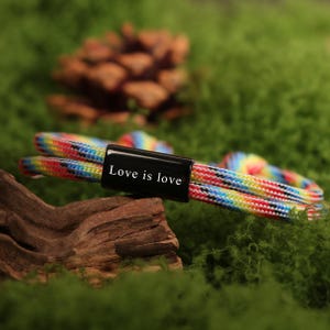 May include: A colorful bracelet with a black clasp. The bracelet features a rainbow pattern of red, orange, yellow, green, blue, and purple. The black clasp has the words "Love is love" in white.