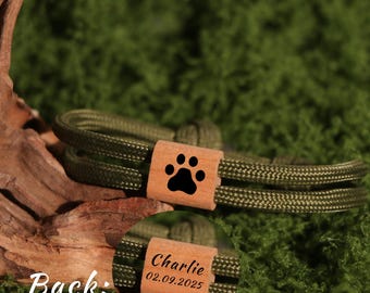 May include: Olive green dog collar with a wooden accent featuring a black paw print. The back of the wooden accent is engraved with the name "Charlie" and the date "02.09.2025". The collar is made of a braided rope material.
