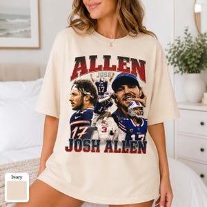 May include: An ivory short-sleeve t-shirt featuring a graphic print of football player Josh Allen. The design includes multiple images of the athlete in a blue and red uniform, with the text "ALLEN" at the top and "JOSH ALLEN" at the bottom.