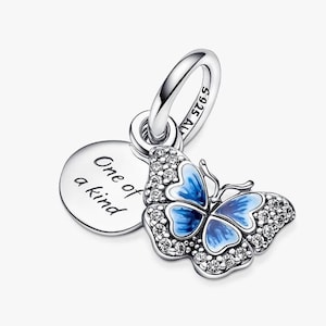 Può includere: Un charm in argento con un design a farfalla. La farfalla ha ali in smalto blu e incastonate con cristalli trasparenti. Un piccolo charm rotondo con la scritta "One of a kind" è appeso accanto alla farfalla.