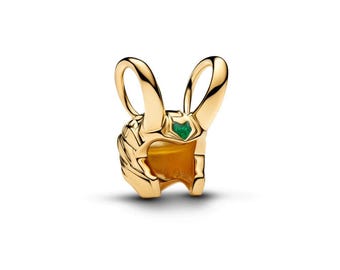 May include: A gold-toned charm shaped like a helmet with two prominent curved horns extending upward. The helmet features a small, triangular green gemstone embedded in the center of the forehead area, with detailed metallic ridges.