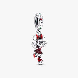 May include: A silver charm featuring Minnie Mouse in a red dress and bow. The charm has a dangling design with a ring at the top, adorned with stars and the brand name. The Minnie Mouse figure is detailed with red enamel.