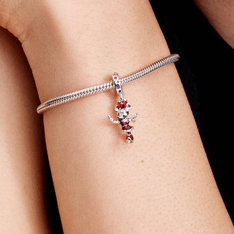 May include: A silver charm bracelet with a Minnie Mouse charm. The charm is red, white, and black with a red bow. The bracelet is a snake chain style.