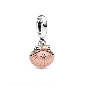May include: A silver and rose gold seashell charm with a small star-shaped gem in the center. The charm is suspended from a silver loop with the word "PANDORA" and the year "2023" engraved on it. The seashell has a textured surface.