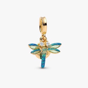 Op de afbeelding: Een goudkleurige bedel in de vorm van een libel, met blauwe en groene geëmailleerde vleugels en een lichaam. De bedel heeft twee kleine heldere stenen en een lus om aan een armband of ketting te bevestigen. Het libellenontwerp is gedetailleerd.