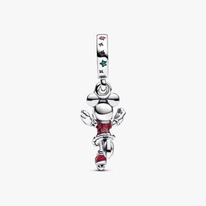 May include: A silver charm featuring a cartoon character in a red dress and hat. The charm has a Mickey Mouse head design and is decorated with red and green stars. The charm is suspended from a silver loop.