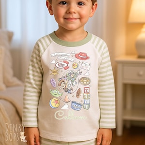 May include: A child's pajama top with long sleeves, featuring a light green and white striped pattern. The front displays a colourful Toy Story graphic and the name "Callum". The neckline is a light green colour.