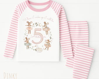 May include: Pink and white striped pajama set. The long-sleeved top features a white body with a pink neckline and sleeves. The front of the top has a graphic of ballet mice and the number 5. The matching pants are pink and white striped.
