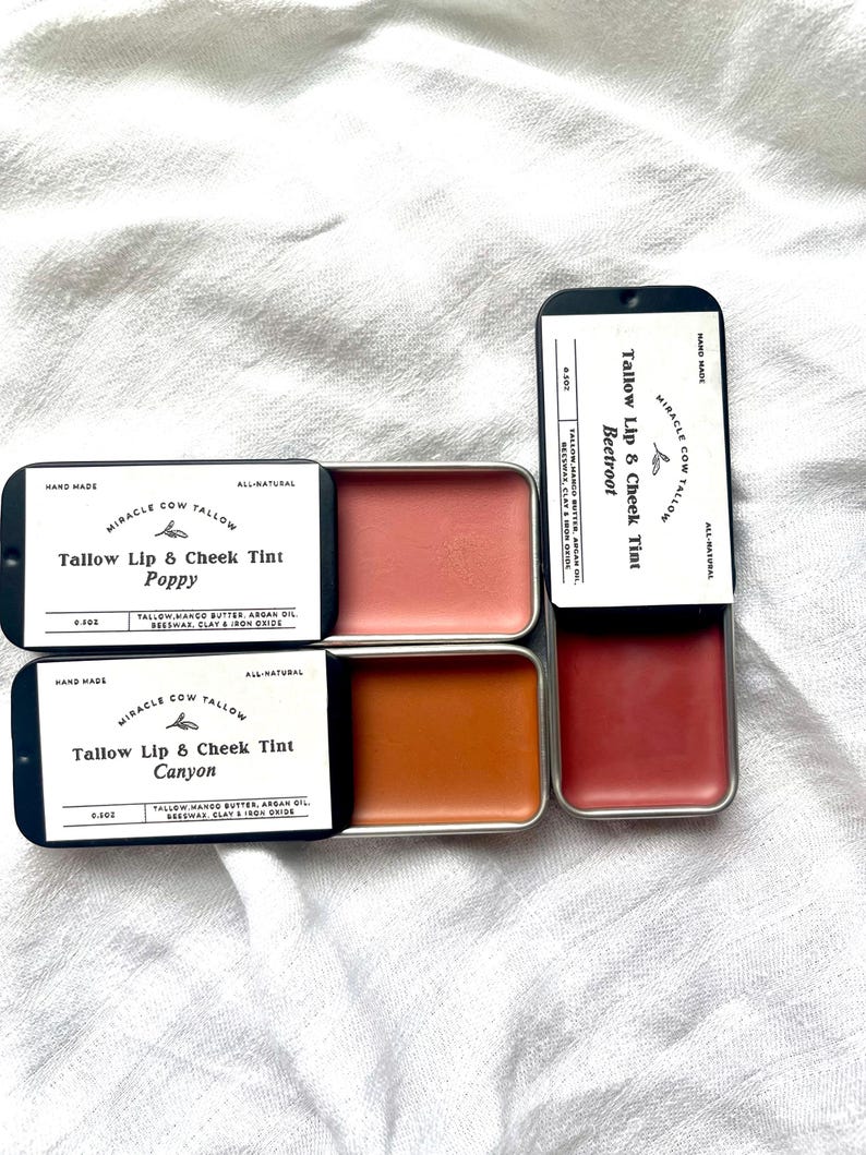 K&ouml;nnte beinhalten: Vier kleine, rechteckige Dosen mit Miracle Cow Tallow Lippen- und Wangenfarben. Die Farbt&ouml;ne sind in Korallen-, Orange- und Rott&ouml;nen gehalten. Jede Dose ist mit dem Produktnamen und den Inhaltsstoffen beschriftet. Die Farbt&ouml;ne Poppy, Canyon und Beetroot sind sichtbar.