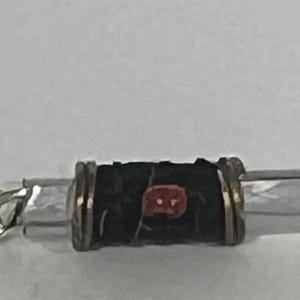 Puede incluir: Primer plano de un pendiente plateado con un cierre de pl&aacute;stico transparente. El pendiente presenta una cuenta cil&iacute;ndrica negra con un acento rojo y cuentas rectangulares transparentes.