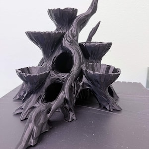 May include: A dark gray, tree-shaped decorative item with multiple small, bowl-like platforms. The sculpture has a textured, carved appearance with a natural, organic aesthetic. The design includes several openings and a prominent, upward-reaching branch.