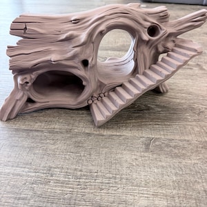 May include: A light brown, hollowed-out log structure featuring a textured bark surface, a large central opening, a smaller side cavity, and a set of stairs leading up to the top of the log. The object is molded with realistic wood grain details.