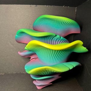 May include: An abstract sculpture in a layered design with a gradient of colours. The piece features green, yellow, pink, and blue. The form appears organic, with a textured, ribbed surface. The artwork is set against a dark background.