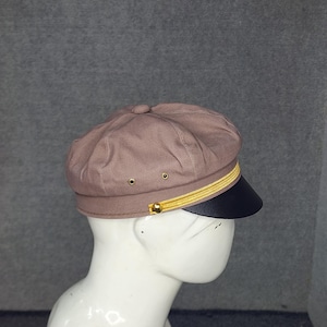 May include: A brown newsboy cap with a black brim and gold trim. The cap has a rounded crown and a structured design. The hat is displayed on a mannequin head.