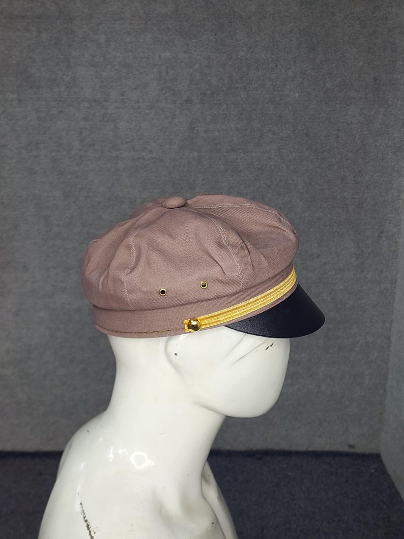 May include: A brown newsboy cap with a black brim and gold trim. The cap has a rounded crown and a structured design. The hat is displayed on a mannequin head.