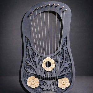 May include: A dark gray lyre with a floral design and gold-colored tuning pegs. The instrument features a carved floral pattern and three flower-shaped sound holes. The strings are a light gold color, and the lyre is set against a dark gray background.