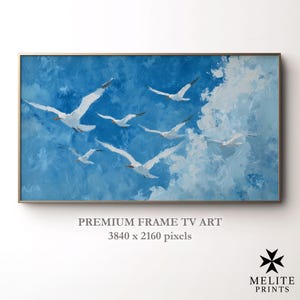 以下が含まれることがあります： 青い空と白い雲を背景に、白い鳥が飛んでいる絵画が描かれた額入りのアートワーク。長方形のアートワークは、金色のフレームが付いています。「PREMIUM FRAME TV ART」と「3840 x 2160 pixels」の文字が下部にあります。