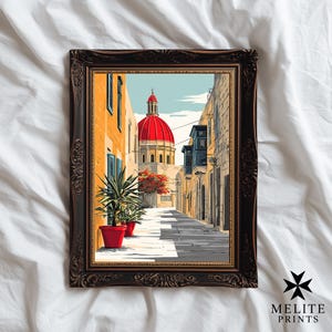 May include: Framed art print depicting a European street scene with a red-domed building. The artwork features a narrow street lined with buildings in shades of yellow and tan. Red flower pots and a decorative frame complete the image.