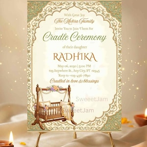 Puede incluir: Una invitación a una ceremonia de cuna, con un marco decorativo y una ilustración de cuna de madera. El texto incluye el nombre "RADHIKA", la fecha, la hora y la información de RSVP. La invitación se muestra en un pequeño caballete dorado.