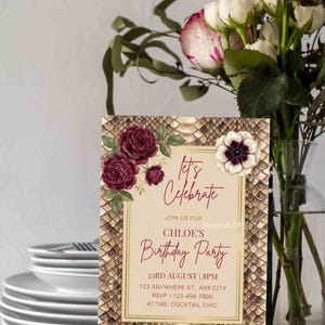 K&ouml;nnte beinhalten: Eine Geburtstagseinladung mit Schlangenmuster und floralen Akzenten. Auf der Einladung steht "Let's Celebrate" und enth&auml;lt Party-Details. Eine Vase mit Blumen und ein Stapel Teller befinden sich im Hintergrund.