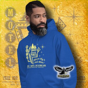 Może przedstawiać: Bordowy sweter z kapturem z grafiką w stylu retro przedstawiającą znak motelu z napisem "Frozen Pines Motel" oraz tekstem "Make your way to  Dave's Shrine!"  i "Free HBO Right Off".