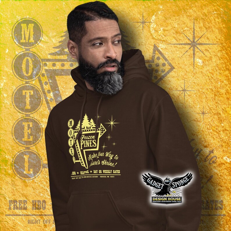 Może przedstawiać: Brązowa bluza z kapturem z grafiką vintage'owego znaku motelu. Znak głosi "Frozen Pines Motel" i zawiera tekst "Make your way to Lars's Shrine!" Grafika jest w kolorze ż&oacute;łtym i wykorzystuje czcionkę w stylu retro. Bluza ma kieszeń kangurzą i kaptur ze sznurkiem.