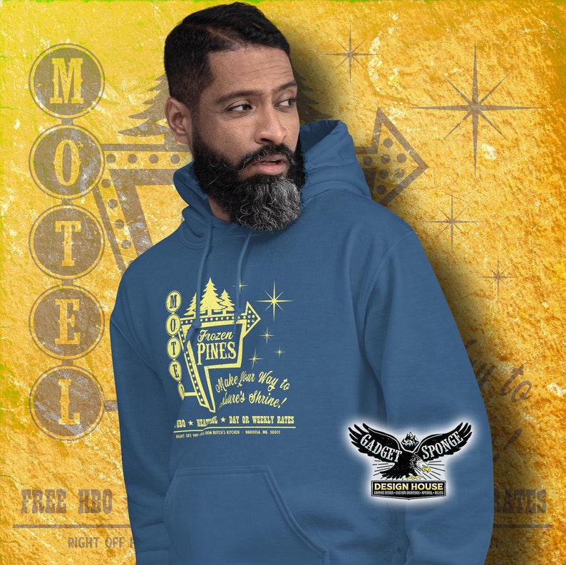 Może przedstawiać: Niebieska bluza z kapturem z grafiką vintage'owego znaku motelu z tekstem "Frozen Pines" i sloganem "Make your way to Dave's Shrine!" Znak jest ż&oacute;łty z białymi gwiazdami i białą obw&oacute;dką. Tekst na bluzie jest ż&oacute;łty.