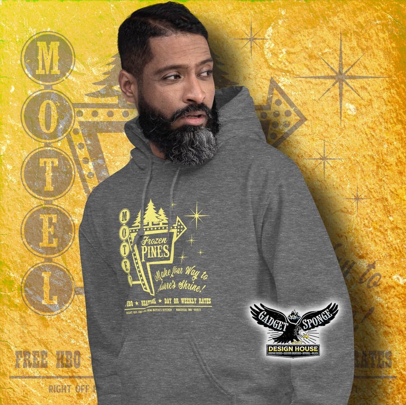 Może przedstawiać: Szara bluza z kapturem z ż&oacute;łtym nadrukiem przedstawiającym vintage'owy znak motelu z napisem "Frozen Pines Motel" oraz tekstem "Make your way to Love's Shrine!" i "Day or Weekly Rates". Nadruk zawiera r&oacute;wnież gwiazdę i sosnę. Bluza ma czarno-białe logo na rękawie z napisem "Gadget Sponge Design House".