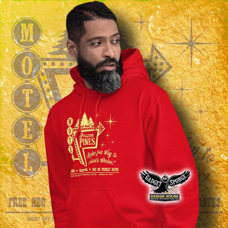 Może przedstawiać: Czerwona bluza z kapturem z nadrukiem w kolorze złotym przedstawiającym vintage'owy znak motelu z napisem "Frozen Pines" oraz tekstem "Make your way to Stan's Shrine!" i "Daily or Weekly Rates". Grafika zawiera r&oacute;wnież gwiazdę i strzałkę wskazującą kierunek. Bluza ma kieszeń kangurkę i kaptur ze sznurkiem.