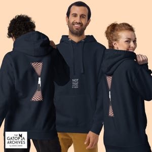 May include: A dark navy blue hooded sweatshirt featuring a front graphic with the text NOT EVERYTHING THAT WATCHES IS SEEN. The back displays a graphic of a cat silhouette between two red and white chevron patterned shapes on a dark background.