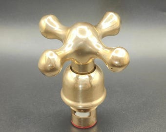Peut inclure: Un robinet en laiton avec une poignée à quatre bras. La poignée a une finition polie et une base arrondie. La poignée de robinet est un accessoire de plomberie et est probablement destinée à un évier ou une baignoire. Le mot "TAZURRA" est imprimé en bas.