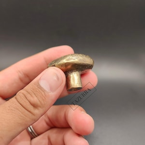 May include: A brass mushroom-shaped cabinet knob. The knob features a textured cap and a cylindrical stem. The finish is a warm, antique gold colour. The knob is designed for use on drawers or cabinets.