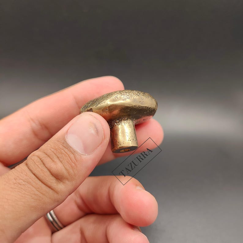 May include: A brass mushroom-shaped cabinet knob. The knob features a textured cap and a cylindrical stem. The finish is a warm, antique gold colour. The knob is designed for use on drawers or cabinets.