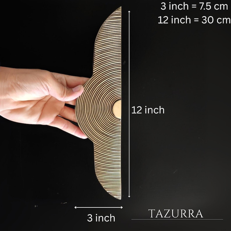 May include: A wooden decorative piece with a unique design. The piece is 12 inches (30 cm) long and 3 inches (7.5 cm) wide. The design features concentric circles on one side and parallel lines on the other. The brand name "TAZURRA" is visible.