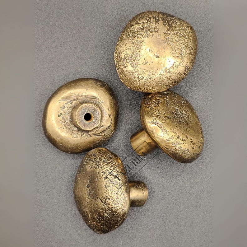 May include: Four antique brass cabinet knobs with a textured, organic design. The knobs have a mushroom-like shape, with a warm, golden hue. One knob is viewed from the back, showing the mounting hardware. The other three knobs are viewed from the front.