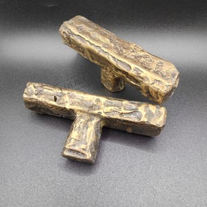 May include: Two bronze cabinet pulls with a textured, organic design. The pulls have a rectangular bar shape with a T-shaped base. The finish has a rustic, aged appearance, suggesting a vintage or antique style. Suitable for furniture or cabinetry.