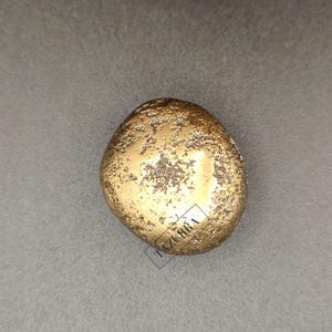 May include: A golden, irregularly shaped decorative object with a textured surface. The object has a rough, pitted appearance and is set against a grey background. The object appears to be made of metal.